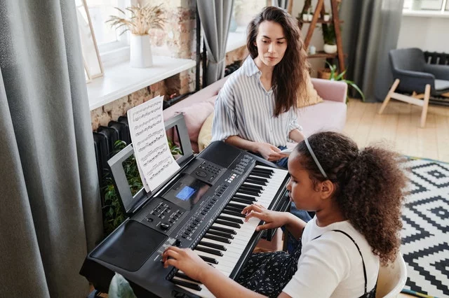 girl practicing piano with tutor